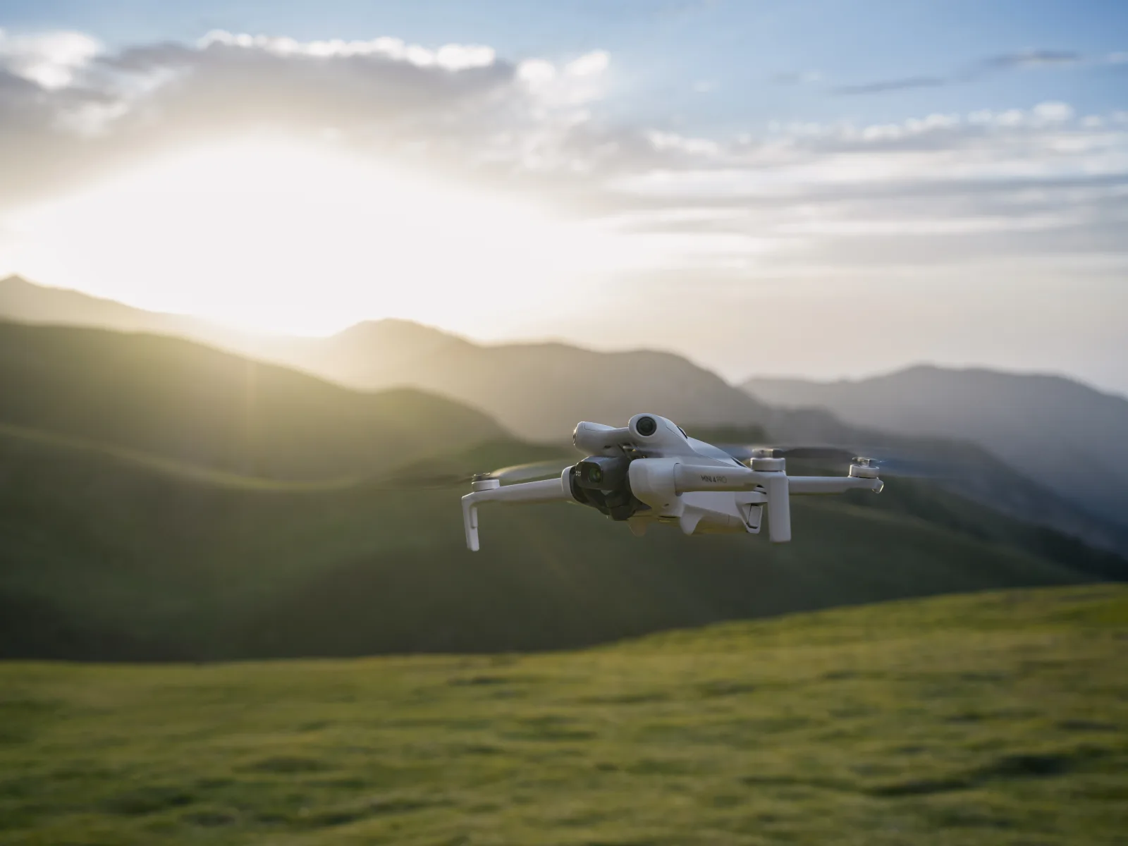 Compact DJI Mini 4 Pro camera drone flying over a mountain landscape