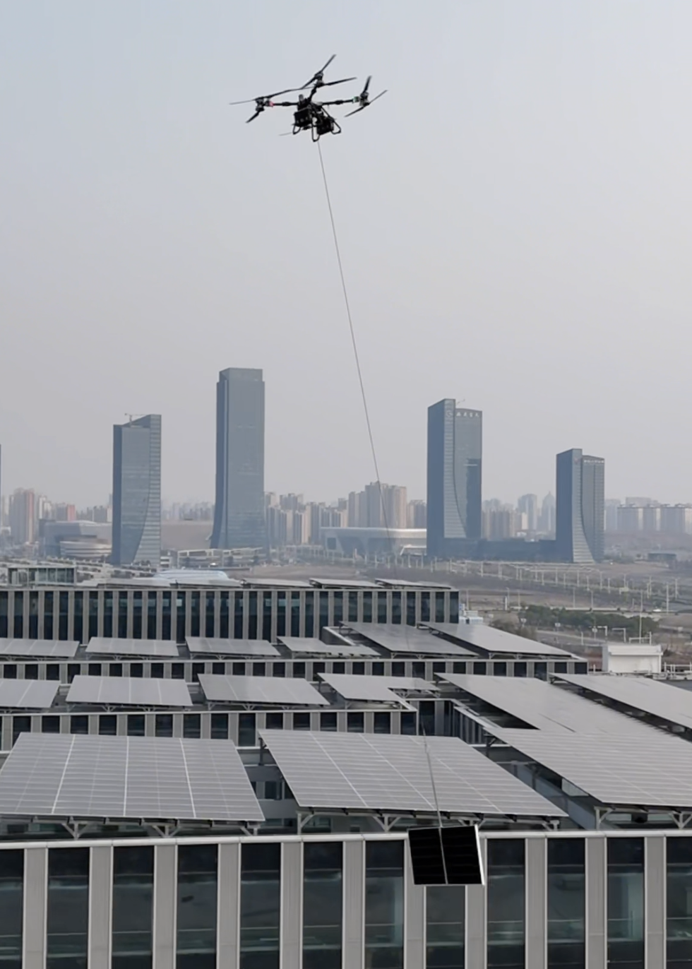 Cargo drone moving a panel over a rooftop PV district