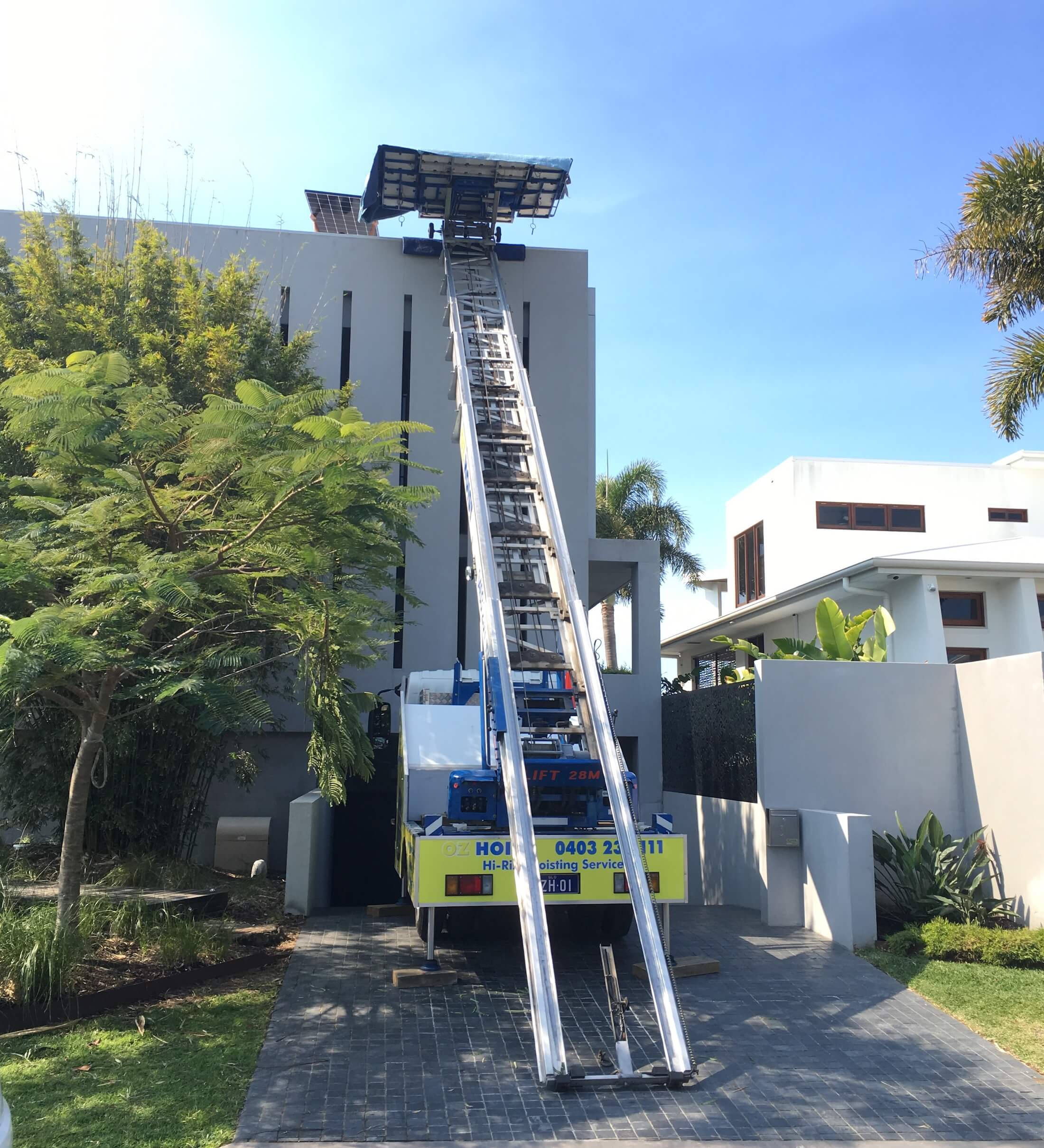 Truck-mounted ladder hoist lifting materials to a modern rooftop